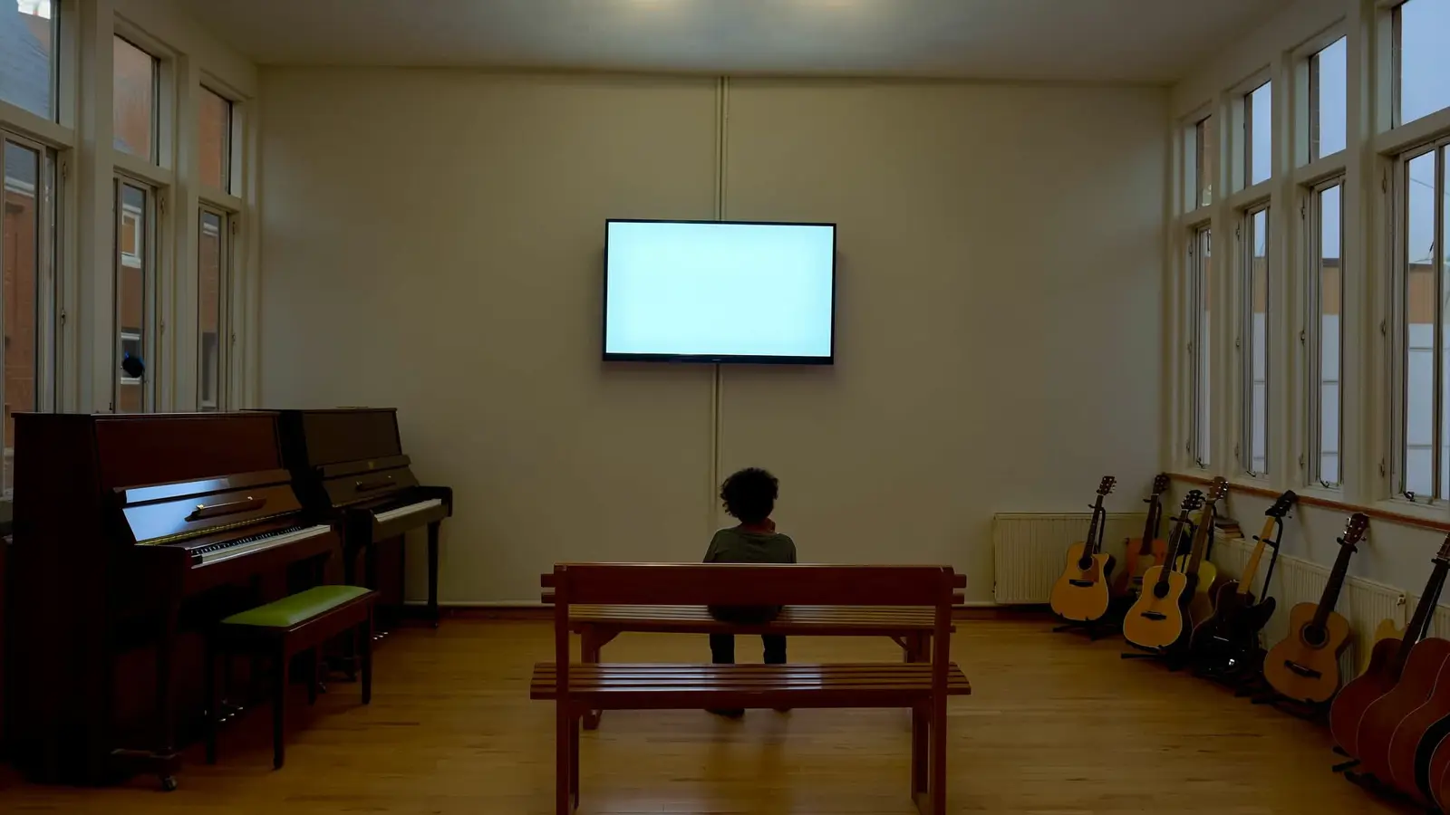 Wartebereich einer Musikschule mit Klavieren und Gitarren, an der Wand hängt ein eingeschalteter Bildschirm